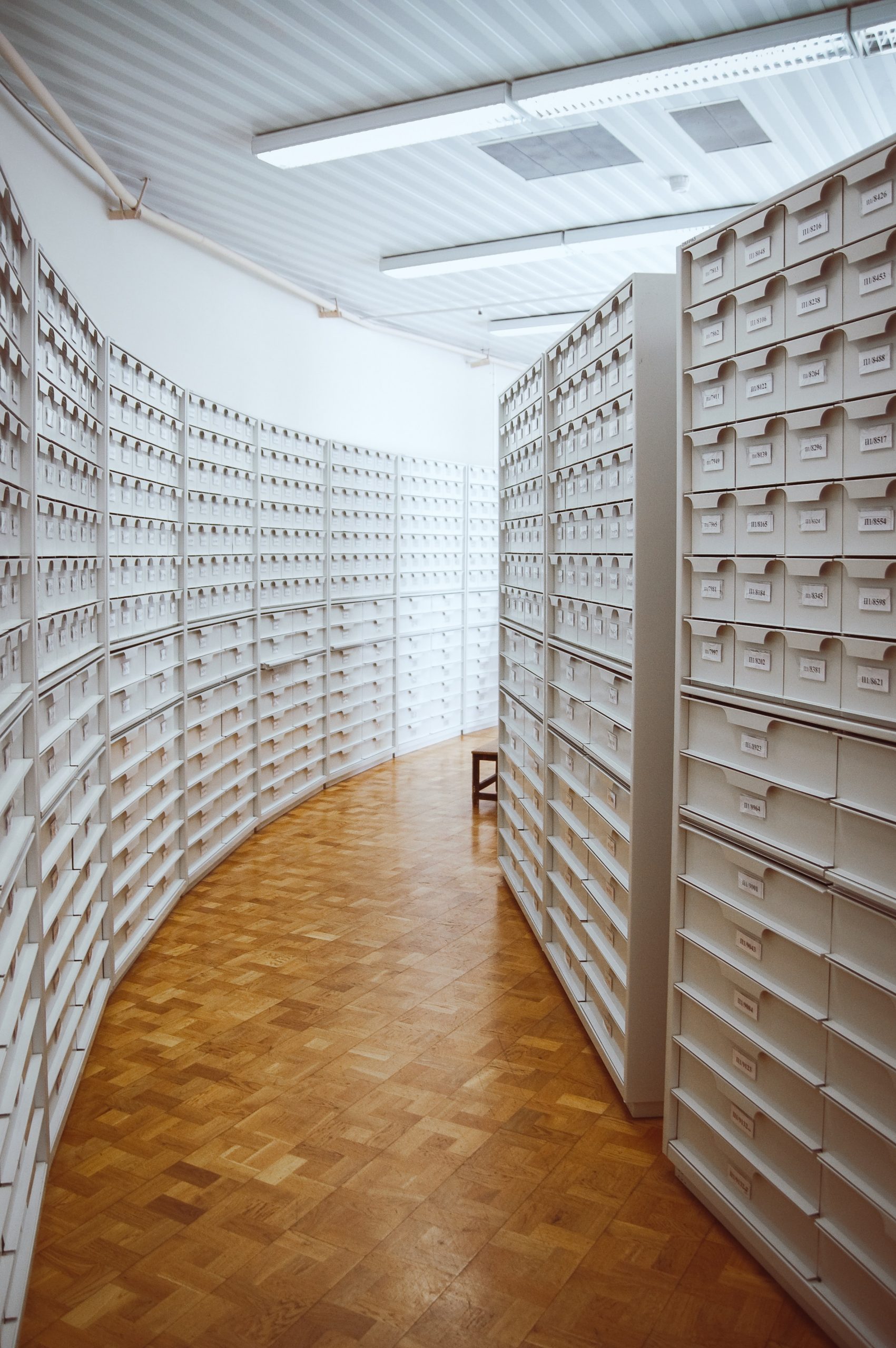 A picture of a curved hallway, both sides filled with white filing cabinets.